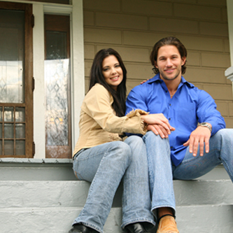 Young couple sitting on the stairs outside of their home.