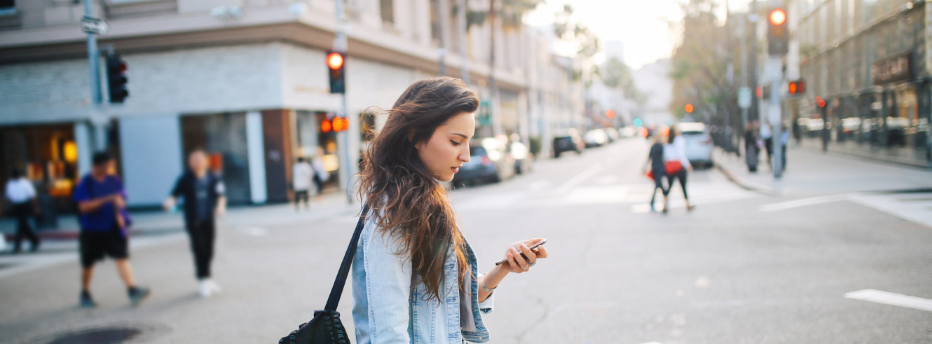 Young woman crossing an intersection. She is looking down at her phone. 