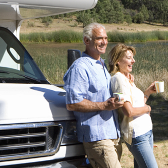 An older couple standing outside with coffee mug leaning against an RV.