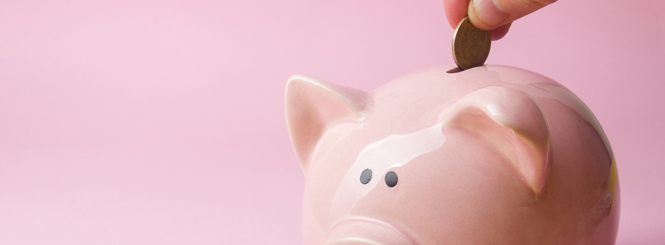 Hand placing a coin in a pink piggy bank.
