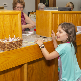 Young girl standing at a bank teller window with her eyes on a basket of candy.