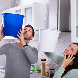 Couple holding buckets to catch water falling from the ceiling. 